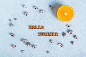 Concept hello summer text, half an orange and seashells on a blue background top view photo