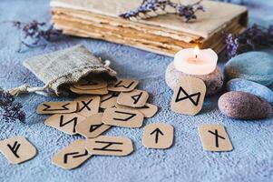 Fortune telling cardboard runes scattered from a bag, a candle, an old book and stones on the table photo