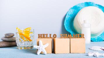 Concept hello summer text on cubes on cocktail background, sunblock and hat on table photo