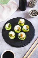 Vegetarian sushi rice, carrots and green onions wrapped in cucumber on a slate board vertical view photo