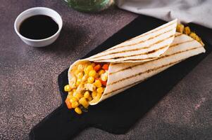 Appetizing burrito in a tortilla made of chicken, corn and peppers on a slate board photo