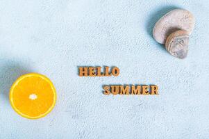 Concept hello summer text, half an orange and stones on a blue background top view photo