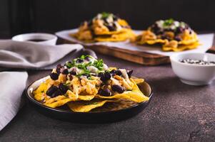 Mexican nacho chips baked with chicken, black beans and cheese on a plate on the table photo