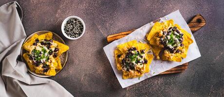 Mexican baked nachos with chicken, black beans and cheese on a board top view web banner photo