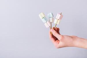 Marshmallow candy kabobs on skewers holding in a hand photo