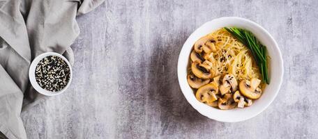 Asian soup with rice noodles, mushrooms and green onions in a bowl top view web banner photo