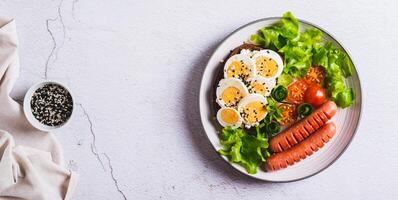 Plate with sausages, egg sandwich, tomatoes and lettuce leaves on the table top view web banner photo