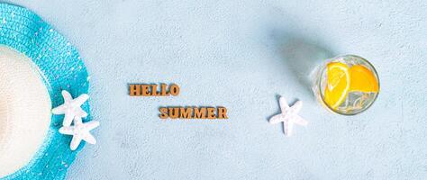 Concept hello summer text, hat, cocktail with orange and starfish on blue top view web banner photo