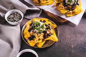 Mexican baked nachos with chicken, black beans and cheese on a plate on the table photo