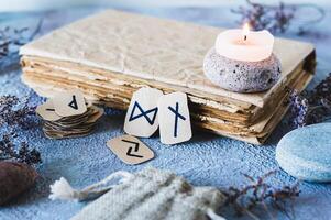 Fortune telling cardboard runes next to an old book, a candle and stones on the table photo