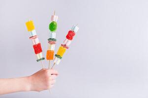 Gummy candy kabobs on skewers holding in a hand photo