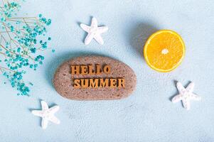 Concept hello summer text on stone, orange, starfish and seashells on blue background top view photo