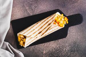 Close up of mexican Burrito with corn, chicken and peppers in a tortilla on a slate board top view photo