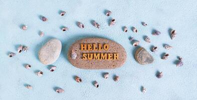 Concept hello summer text on stone surrounded by seashells on blue background top view web banner photo