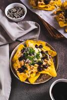 Mexican baked nachos with chicken, black beans and cheese on a plate on the table vertical view photo