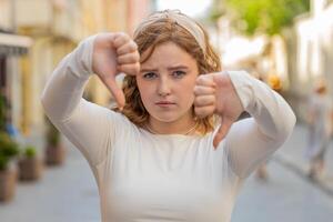 Upset redhead woman showing thumbs down sign disapproval dissatisfied bad work mistake in city photo