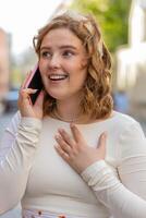 Happy young woman having remote conversation talking on smartphone good news gossip in city street photo