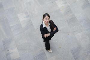 exitoso y confidente joven asiático mujer de negocios en pie al aire libre en un ciudad pavimento foto