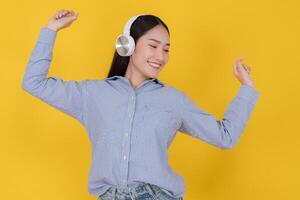 Joyful young woman dancing with headphones on yellow background photo