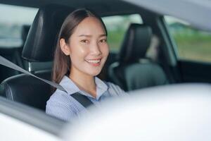 Smiling young woman sitting in the driver's seat, confidently holding the steering wheel of a car with a bright and cheerful expression, highlighting safe and enjoyable driving photo