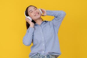 Joyful young woman dancing with headphones on yellow background photo