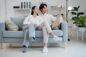 Couple relaxing on couch adjusting air conditioner with remote control photo