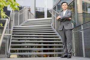 Confident asian businessman with crossed arms wearing a stylish gray suit showcasing leadership qualities and determination photo