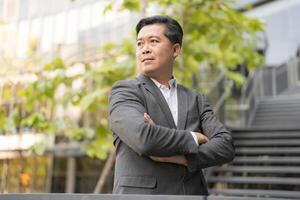 Confident asian businessman with crossed arms wearing a stylish gray suit showcasing leadership qualities and determination photo