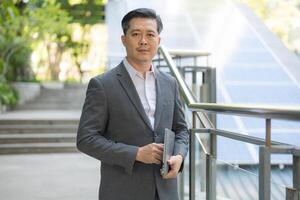 Confident businessman in a smart suit is holding with his laptop while standing outdoor in a modern urban setting photo