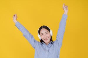 Joyful young woman dancing with headphones on yellow background photo