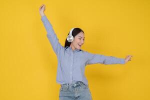 Joyful young woman dancing with headphones on yellow background photo