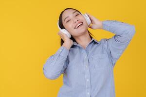 Joyful young woman dancing with headphones on yellow background photo