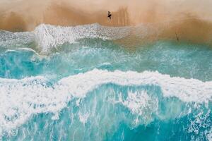 Surfer on tropical sandy beach with blue transparent ocean and waves. Aerial view photo