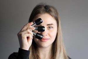 un rubia niña sostiene botellas de uña polaco en su mano. de cerca foto