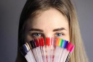 un rubia niña sostiene en su mano un paleta con muestras de uña pulimentos grande selección de gel polaco colores. color monitor en el anillo. de cerca foto