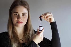 A blonde girl holds open nail polish in her hand. Close-up photo