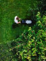 Caucasian man pushing lawn mower for cutting green grass in garden with sunlight at summer season. Aerial view. Housework and lifestyle concept. photo