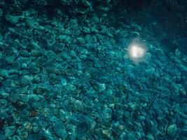 Blue ocean in sunny day, aerial view. Transparent sea background with stone sea bottom. Top view photo