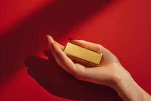 Female hand with fashionable manicure holds a gold bar on a red background photo