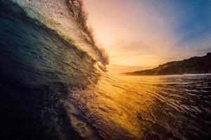 Barrel wave crashing in ocean on warm sunset or sunrise. photo