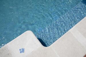 borde de un nadando piscina con blanco losas, verano hora foto