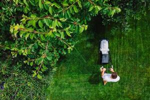 Man pushing lawn mower for cutting grass in garden at summer. Aerial view. photo