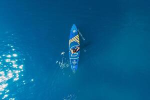 July 15, 2021. Anapa, Russia. Athletic woman on stand up paddle board at blue sea. Surfer woman on Gladiator sup board in sea. Aerial view, top view photo