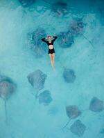 Woman swimming with stingrays in Maldives. Sting ray fishes and woman swimming in blue sea, Aerial view photo