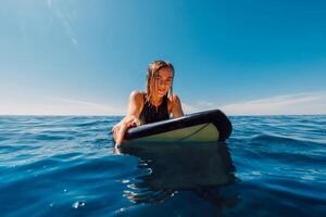 retrato de navegar niña en tabla de surf. hermosa rubia mujer Mira a cámara en línea arriba. tablista en Oceano foto
