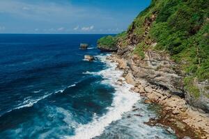 Coastline with rocks and transparent ocean with waves in Bali. Aerial view. photo
