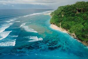 Aerial view of coastline with turquoise ocean and tropical beach under cliffs in Bali. photo