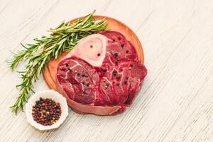 Fresh piece of meat large beef steak on the bone ossobuco with pepper, rosemary on the board photo