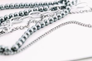 A necklace of gray beads with chain decorations on a white aesthetic background. photo