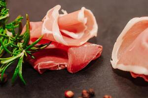 Pieces of dried pork jamon prosciutto with rosemary on a black board. photo